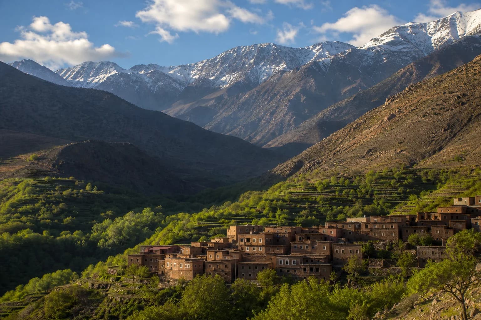 An Amazigh village in a green valley beneath the snow-dusted High Atlas mountains